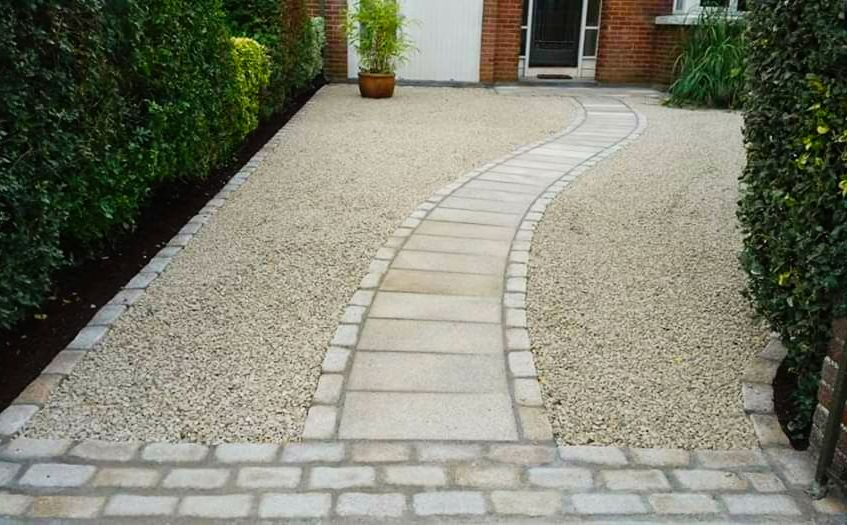 Curved stone pathway through gravel beside a green hedge